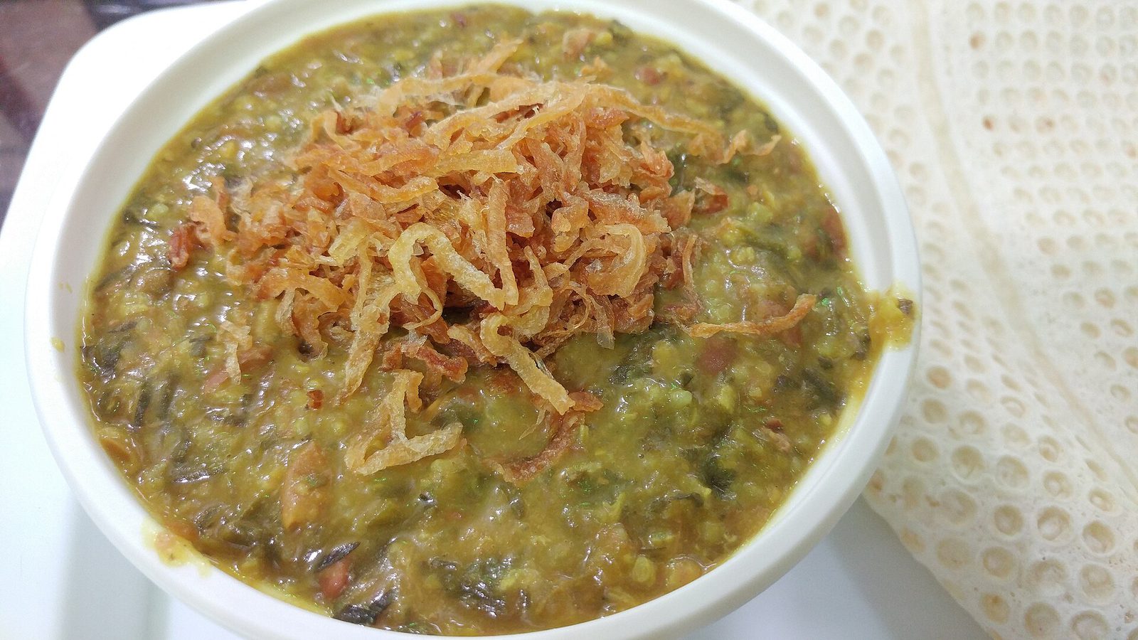 Bol de âsh épais aux herbes et légumes secs, garni d'oignon frit
