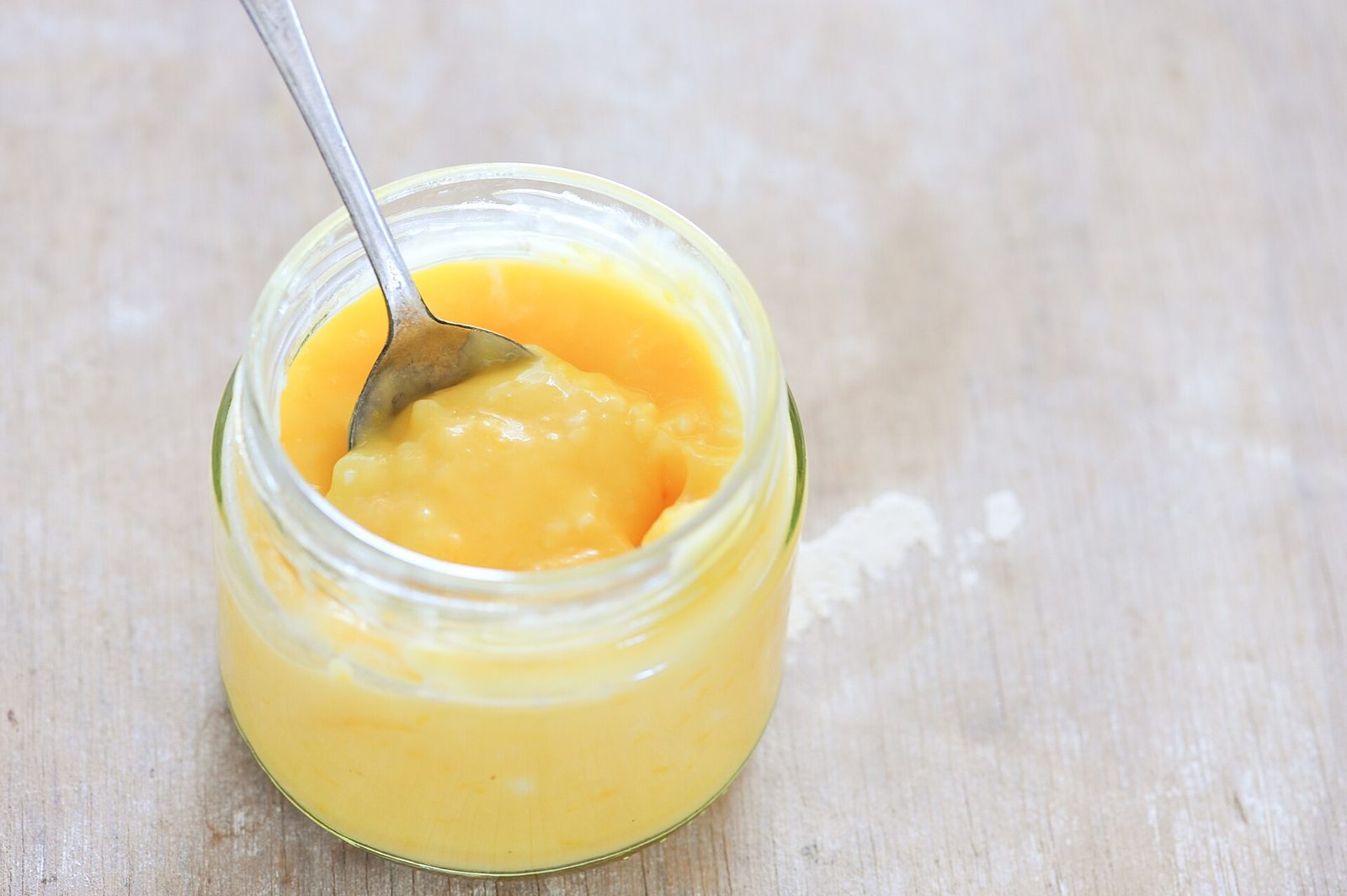 Crème de citron jaune vif dans un pot en verre, une cuillère plantée dedans