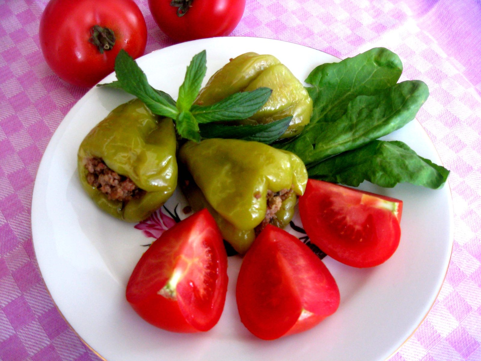 Poivrons verts farcis à la viande dans une assiette, avec des quartiers de tomate et de la menthe fraîche