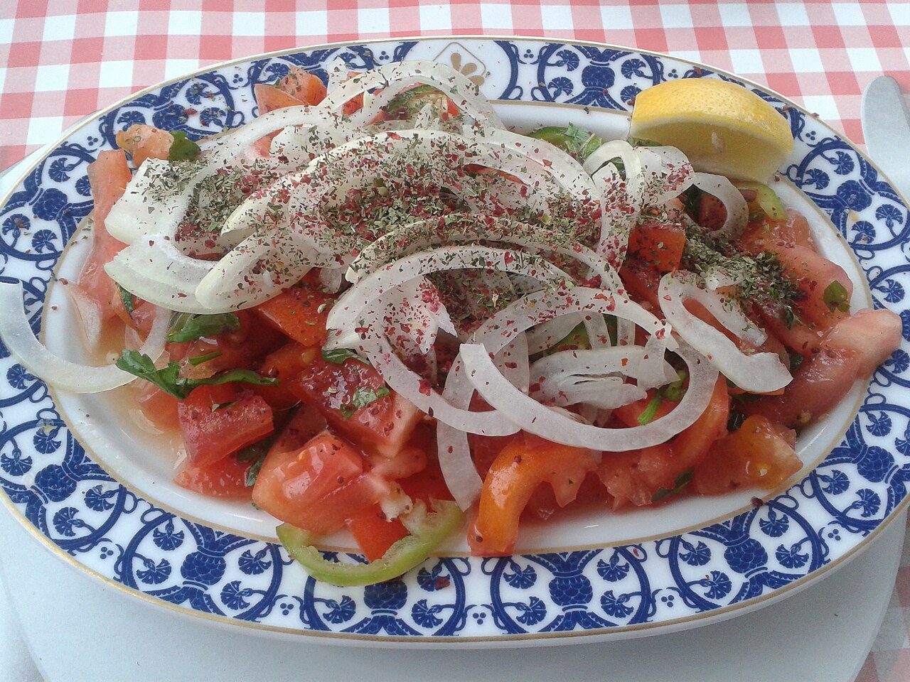 Salade de tomates en quartiers, anneaux d'oignon crus, sumac et menthe séchée, sur un plat ovale