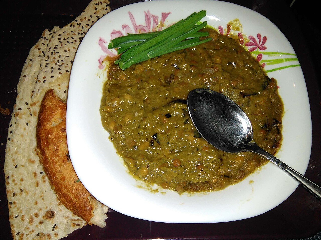 Assiette d'âsh vert sombre aux légumes secs, avec du pain plat et de la ciboule
